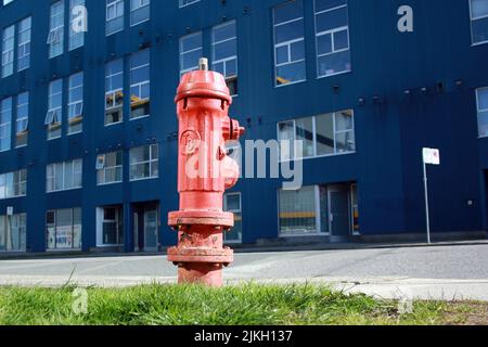 Ein alter roter Hydrant auf dem Gehsteig für den Notzugang zum Feuer - Gebäude im Hintergrund Stockfoto