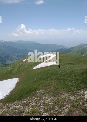 Die felsige Bergkette mit dem grünen Feld, das teilweise von Schnee bedeckt ist, in Teghenis, Armenien Stockfoto