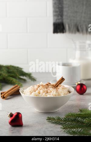 Skandinavischer Reisbrei mit Zimt in einer Schüssel, umgeben von Weihnachtskugeln. Frühstück am Heiligabend. Stockfoto