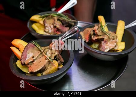 Eine Nahaufnahme von Schüsseln mit Rindfleisch und gebratenen Kartoffeln mit Sauce auf dem Tablett bedeckt Stockfoto