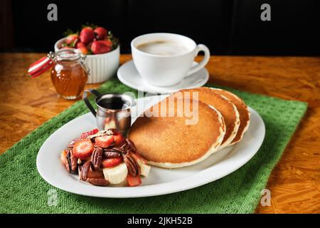 Eine Nahaufnahme des perfekten Frühstücks mit hausgemachten Pfannkuchen, Obst und einer Tasse Kaffee Stockfoto
