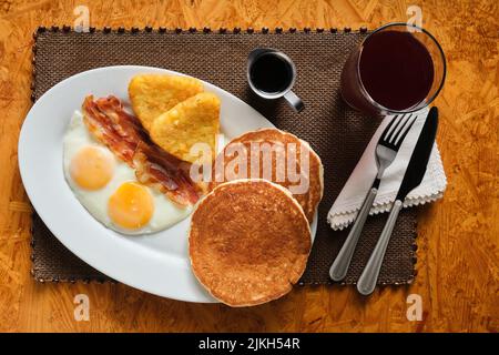 Ein Blick von oben auf ein traditionelles amerikanisches Frühstück mit Pfannkuchen, Speck, Eiern und Kartoffelrösti Stockfoto