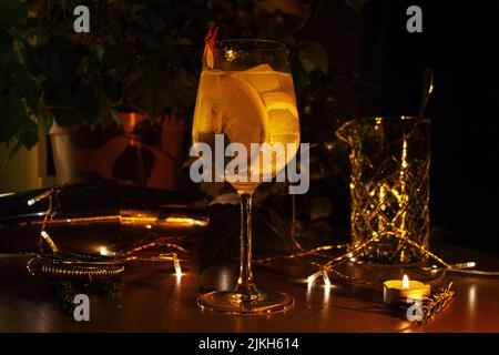 Eine Nahaufnahme eines orangefarbenen Gin Tonic-Cocktails in einem Weinglas, das mit Kerzen und Lichtern dekoriert ist Stockfoto