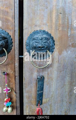 Eine alte Holztür mit einem Metallgriff in Form eines Löwenkopfes mit Ring und einem aufgehängten chinesischen Accessoire Stockfoto