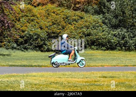 Seitenansicht pan shot of man riding classic light Green innocenti lambretta 125 Scooter Moped at weston Park classic car show 2022 Stockfoto