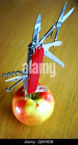 Ein vertikaler Schuss eines Multitool-messers der schweizer Armee, das in einen Apfel gestochen wurde Stockfoto