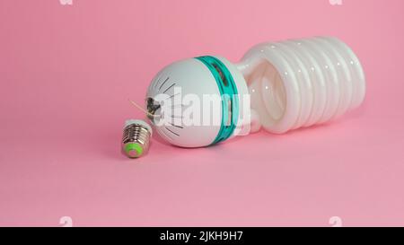 Eine kaputte Energiesparlampe auf einem rosa pastellfarbenen Hintergrund Stockfoto