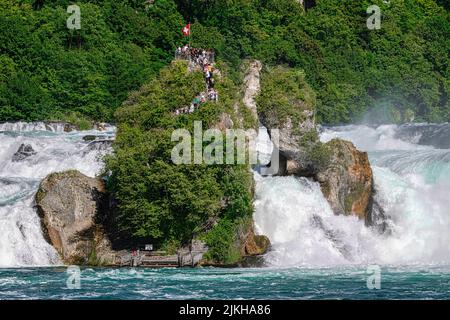 Die Menschen bewundern die Rheinfälle vom Boot aus, das Touristen auf die exklusive Terrasse mitten im Wasserfall bringt. Stockfoto