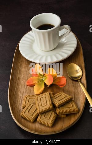 Tasse Kaffee mit Gebäck, dekoriert mit Frühlingsblumen auf dunklem Hintergrund. Stockfoto