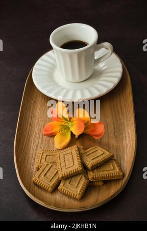 Tasse Kaffee mit Gebäck, dekoriert mit Frühlingsblumen auf dunklem Hintergrund. Stockfoto