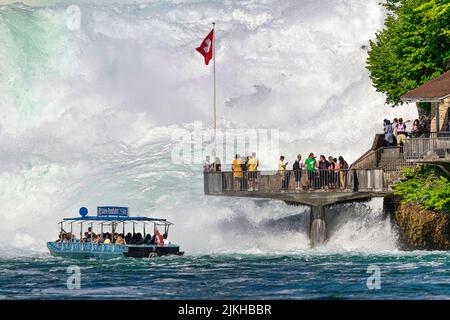 Die Menschen bewundern die Rheinfälle vom Boot aus, das Touristen auf die exklusive Terrasse mitten im Wasserfall bringt. Stockfoto