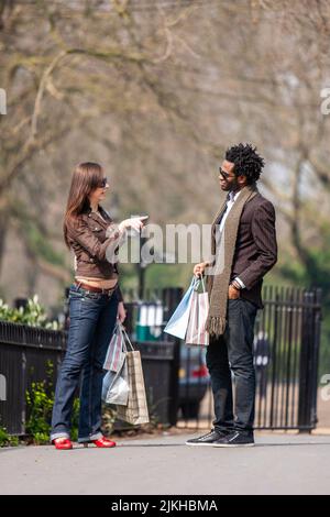London Shopper; Shop Talk. Ein junges gemischtes Rennpaar diskutiert nach einem Einkaufstag über ihre Pläne. Aus einer Reihe von Bildern. Stockfoto