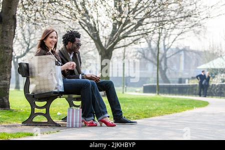 London Shopper; eine Pause machen. Ein junges gemischtes Rennpaar genießt sich in einem Londoner Park. Aus einer Reihe von Bildern. Stockfoto
