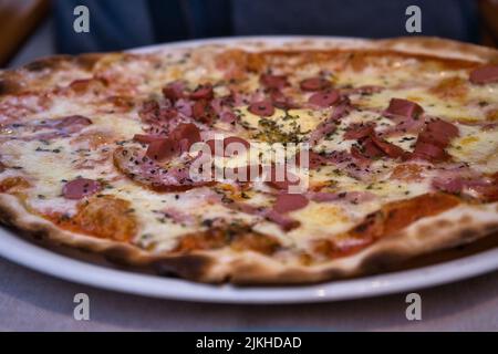 Nahaufnahme einer frischen Pizza mit Wurst, Tomaten und Käse auf einem Restauranttisch. Selektiver Fokus Stockfoto