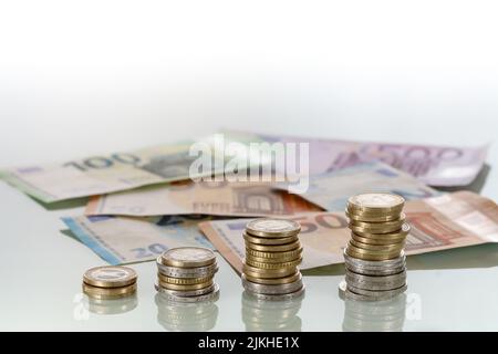 Stapel von Euro-Münzen und Euro-Banknoten auf glänzender Oberfläche Stockfoto