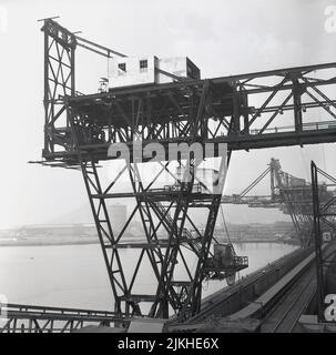 1950s, historische Ansicht einer großen industriellen Ladestruktur neben dem Gezeitenhafen beim riesigen Stahlwerk Abbey Works in Port Talbot, Wales, Großbritannien. Im Jahr 1947 begannen die Planungen für das „Abteiwerk“ – benannt nach dem nahegelegenen Monsterei –, das etwas weiter östlich in Margam errichtet wurde und 1951 eröffnet wurde. Bis zum Jahr 1960s beschäftigte das Abbey-Werk mehr als 20.000 Mitarbeiter und war das größte Stahlwerk in Europa. Heute ist der Hafen einer der wenigen der Welt, der Capesize-Schiffe, die größten Trockenfrachtschiffe, umladen kann. Stockfoto