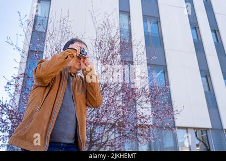 Älterer Mann, der mit seiner alten Filmkamera in der Stadt fotografiert. Stockfoto