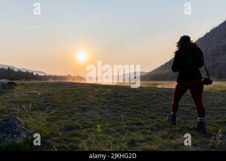 Die Silhouette der Frau mit einer Kamera im Yellowstone National Park bei Sonnenaufgang. Stockfoto