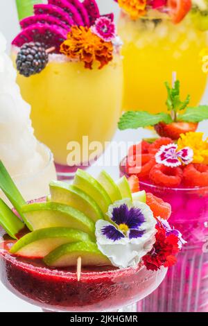 Nahaufnahme von verschiedenen Geschmacksrichtungen von Cocktails zusammen mit Dekoration von Früchten und essbaren Blumen. Stockfoto