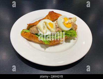 Buttercroissant-Sandwich, gefüllt mit herzhaftem Mayonnaise-Thunfisch, einem Stück frischem Salat und zwei Scheiben hart gekochtem Ei. Stockfoto