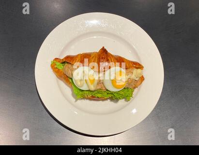 Buttercroissant-Sandwich, gefüllt mit herzhaftem Mayonnaise-Thunfisch, einem Stück frischem Salat und zwei Scheiben hart gekochtem Ei. Stockfoto