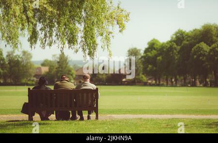 Ein heller Sommertag im Freien mit drei Personen saß auf einer Bank in einem Park umgeben von üppigem Grün Stockfoto