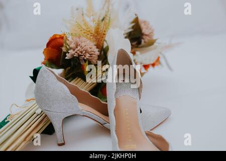 Eine Nahaufnahme eines Paares Brautschuhe und ein Blumenstrauß an einem Hochzeitstag Stockfoto