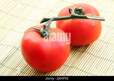 Eine Nahaufnahme von zwei rohen roten Tomaten auf einer Bambusmatte Stockfoto