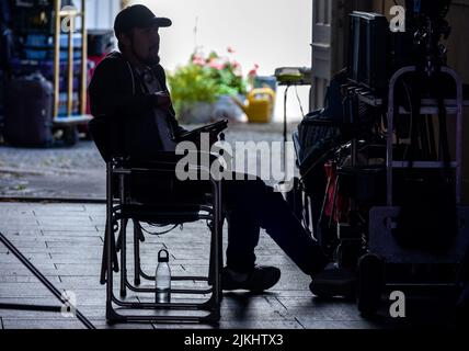 Schwerin, Deutschland. 02. August 2022. Ein Teammitglied sitzt während der Dreharbeiten für die neue ZDF-Serie „Hotel Mondial“ auf dem Regiestuhl. Das imaginäre 4-Sterne-Hotel 'Mondial', das auf eine lange Tradition zurückblicken kann, bildet den Rahmen für das Grundstück. Nach Angaben der Produktionsfirma wird die erste Staffel aus zwölf Episoden bestehen und im nächsten Jahr mittwochs ausgestrahlt. Quelle: Jens Büttner/dpa/Alamy Live News Stockfoto