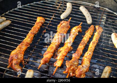 Eine Nahaufnahme von leckeren Shish Kebabs, die auf einem Grill mit kleinen Würstchen daneben kochen Stockfoto