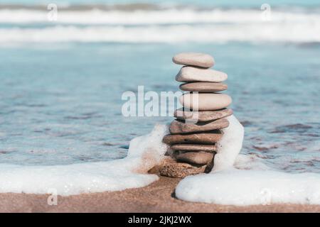 Ein flacher Fokus von Strandsteinen, die auf dem Hintergrund des geschäumten Meeres aufeinander gestapelt sind Stockfoto