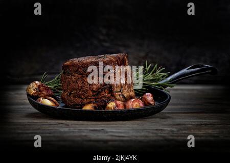 Die magnetische Nahaufnahme des Studios mit frischen Scheiben dickem Steakfleisch mit Knoblauch und Rosmarin auf einem Holzbrett Stockfoto