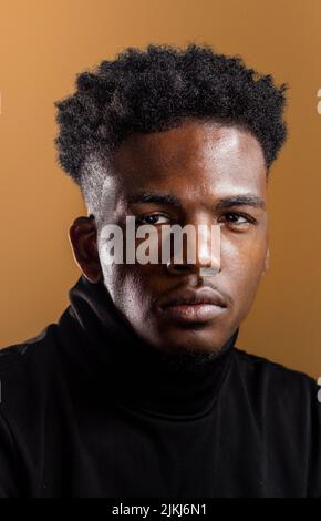 Eine vertikale Aufnahme eines afroamerikanischen Mannes auf dem ockerfarbenen Hintergrund. Stockfoto