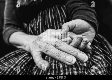 Ein junger Mann hält die faltige Hand einer älteren Frau in Schwarz-Weiß-Tönen Stockfoto