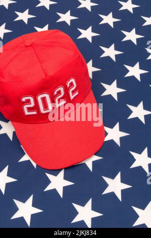 Red MAGA-Typ Hut mit 2022 Datum auf US Stars and Stripes Flagge. Für republikanische Siege bei den Mittelfristwahlen in den USA im November 2022 und der Roten Welle der US-Republikaner. Stockfoto