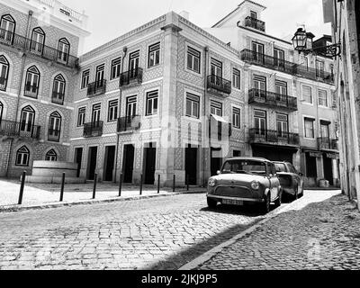 Eine Graustufenaufnahme eines Autos, das auf einer Kopfsteinpflasterstraße in Alfama, Lissabon, geparkt wurde Stockfoto