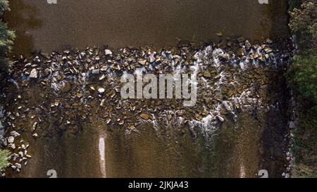 Ein Blick von oben auf einen Pfad aus Kies und Steinen in einem Fluss und Büschen auf beiden Seiten Stockfoto