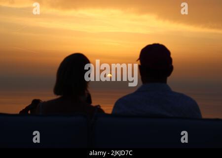 Eine Rückansicht einer Silhouette eines Paares, das den Sonnenuntergang über dem Strand genießt Stockfoto