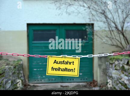 Ein gelbes Schild an einer Kette, mit den deutschen Worten für „Keep Gateway clear“ (Abfahrt frei) vor einem Garageneingang Stockfoto