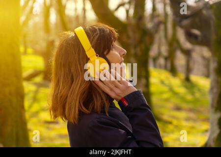 Ein Mädchen, das bei Sonnenuntergang Musik mit gelben Kopfhörern im Wald hört Stockfoto