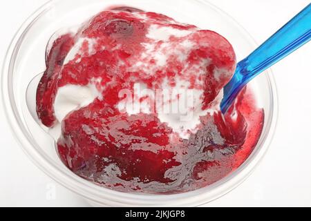 Eine Nahaufnahme von Eis mit Fruchtsauce in einer Plastikschale und einem Löffel auf weißem Hintergrund Stockfoto