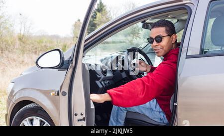 Hübscher junger Hispanic, der sein Auto benutzt und sein Smartphone anschaut Stockfoto