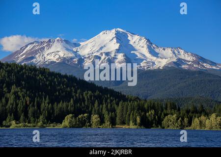 Eine malerische Aussicht auf den Mount Shasta mit einem Vordergrund von Bäumen bedeckten Hügeln und einem Gewässer Stockfoto