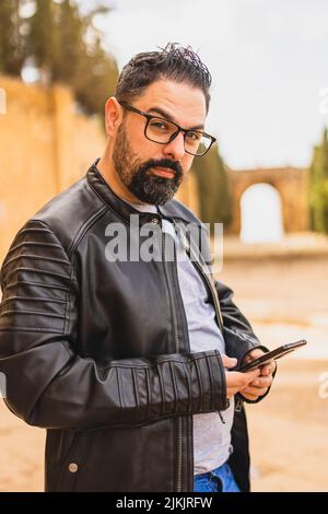 Eine vertikale Aufnahme eines jungen bärtigen Mannes in einer Lederjacke, der sein Telefon benutzte Stockfoto