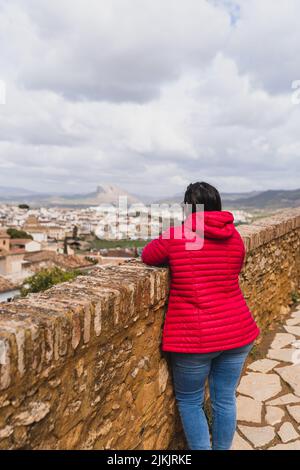 Eine vertikale Aufnahme einer Frau, die mit roten Aufkantung steht und durch die Stadt blickt. Stockfoto