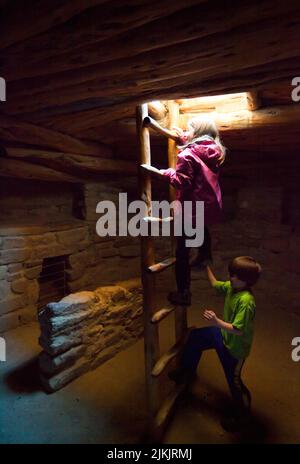 Zwei Kinder besuchen die Ruinen des Spruce Tree House und klettern über eine Holzleiter zur unterirdischen Kiva. Mesa Verde National Park auf dem Colorado Plateau, CO Stockfoto