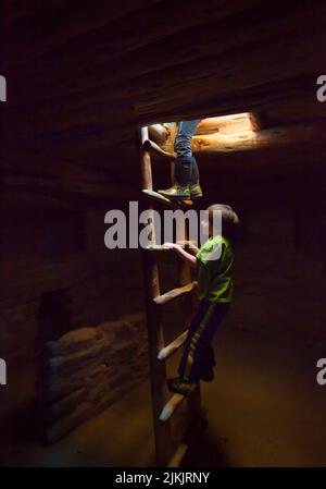 Zwei Kinder besuchen die Ruinen des Spruce Tree House und klettern über eine Holzleiter zur unterirdischen Kiva. Mesa Verde National Park auf dem Colorado Plateau, CO Stockfoto