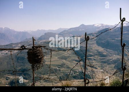 Eine Nahaufnahme einer alten Rolle Stacheldraht hing an einem alten Zaunpfosten. Berge im Hintergrund Stockfoto