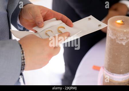 Eine Nahaufnahme der Hände eines Mannes, der die goldenen Eheringe in einem weißen Gehäuse hält Stockfoto