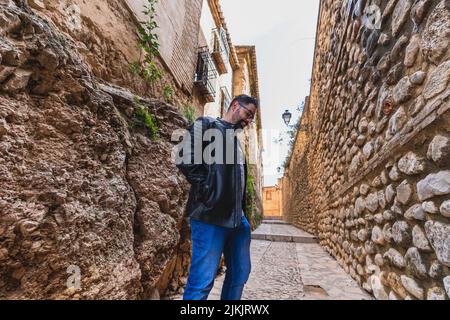 Ein bärtiger Mann in einer Lederjacke und einer Brille, die in einer Gasse posiert Stockfoto